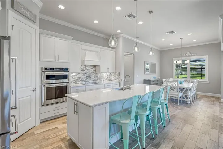 Kitchen with crown molding, backsplash, light wood-style flooring, a center island with sink, and white cabinets