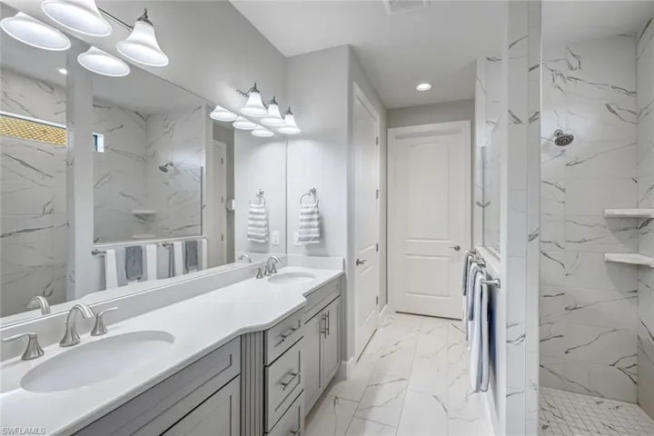 Bathroom featuring marble look tile flooring, a marble finish shower, double vanity, and recessed lighting