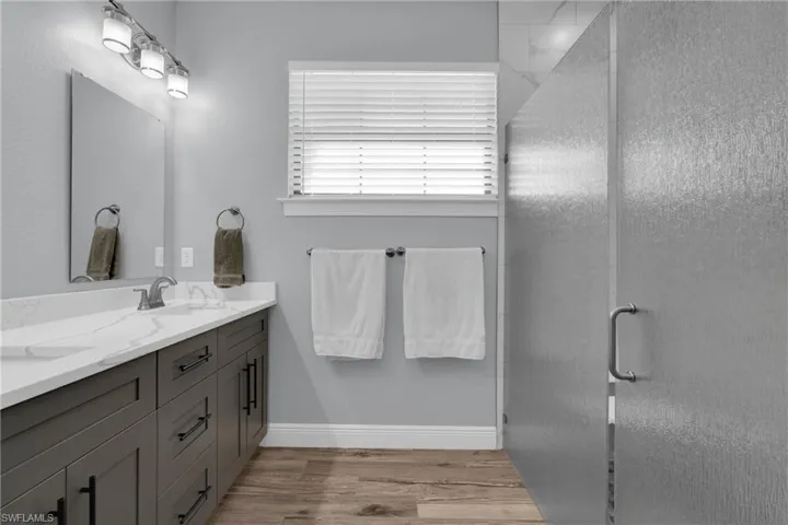 Full bathroom featuring a stall shower, double vanity, and light wood finished floors