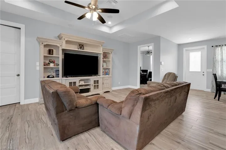 Living room featuring a tray ceiling, a ceiling fan, light wood-type flooring, and recessed lighting