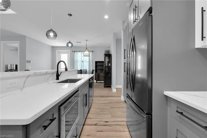 Kitchen with light stone counters, stainless steel appliances, decorative light fixtures, two tone cabinetry, and light wood-type flooring