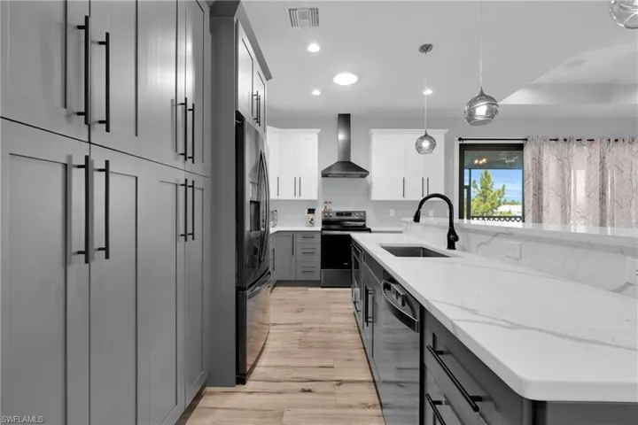 Kitchen featuring stainless steel appliances, decorative light fixtures, two tone color scheme, light stone countertops, and light wood-type flooring