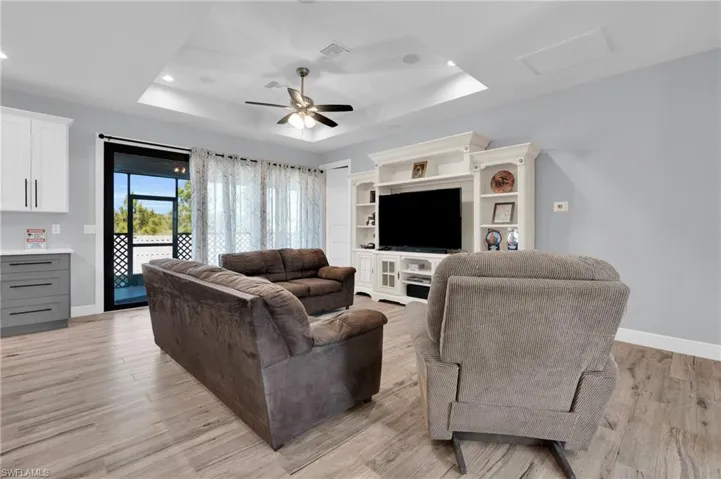 Living area with a ceiling fan, a tray ceiling, light wood finished floors, and recessed lighting