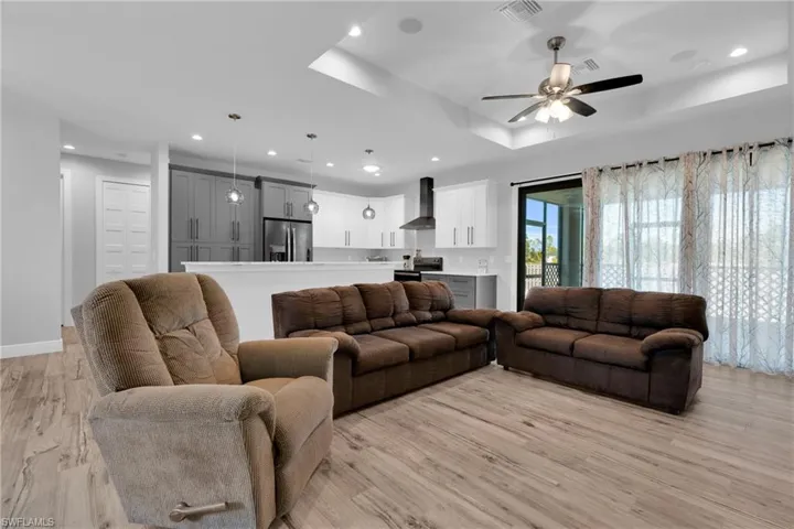 Living room featuring a ceiling fan, light wood finished floors, recessed lighting, and a raised ceiling
