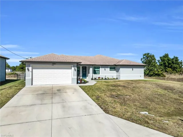 View of front facade featuring a front yard, driveway, an attached garage, stucco siding, and roof with shingles