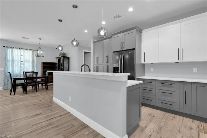 Kitchen featuring dual tone cabinets, decorative light fixtures, an island with sink, stainless steel fridge with ice dispenser, and light wood finished floors