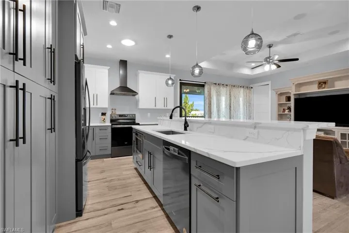 Kitchen featuring two tone cabinets, pendant lighting, stainless steel appliances, light stone counters, and light wood-type flooring