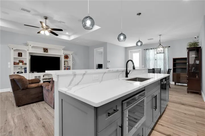 Kitchen featuring gray cabinetry, a center island with sink, pendant lighting, light stone countertops, and a tray ceiling