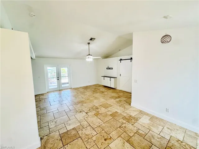 Unfurnished living room featuring a barn door, stone tile floors, ceiling fan, and lofted ceiling