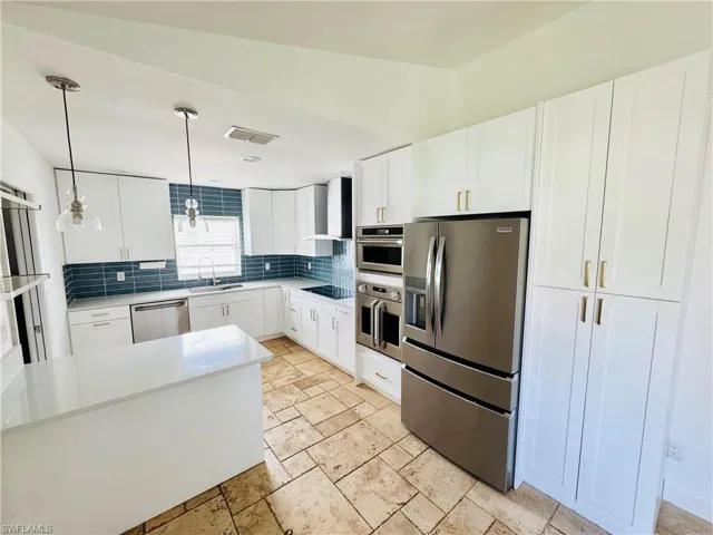 Kitchen featuring stainless steel appliances, decorative backsplash, pendant lighting, light countertops, and wall chimney range hood