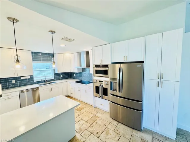 Kitchen featuring stainless steel appliances, backsplash, decorative light fixtures, wall chimney exhaust hood, and white cabinetry