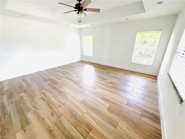 Empty room with a raised ceiling, light wood-style floors, a ceiling fan, and crown molding
