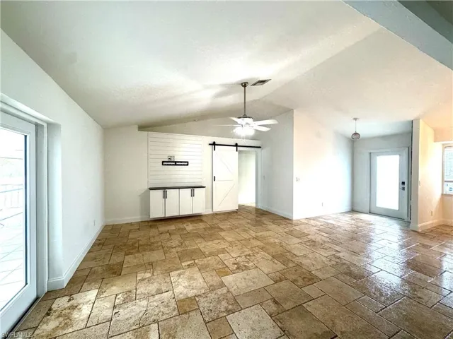 Unfurnished living room featuring a barn door, stone tile floors, lofted ceiling, and a ceiling fan