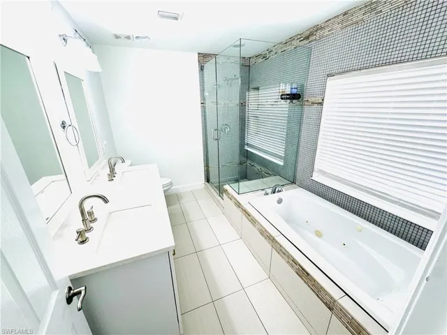 Bathroom with a tub with jets, a stall shower, vanity, and tile patterned flooring