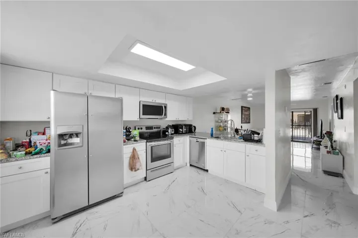 Kitchen with stainless steel appliances, light stone countertops, white cabinetry, a peninsula, and light marble finish flooring