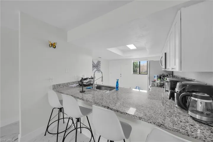 Kitchen featuring a breakfast bar area, light stone countertops, a peninsula, white cabinetry, and stainless steel microwave