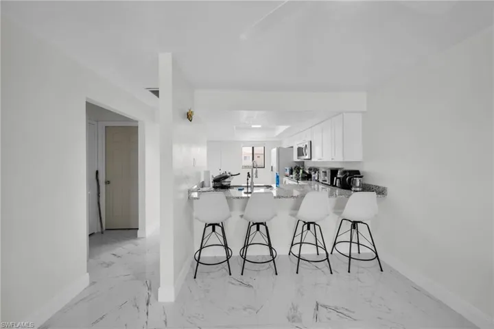 Kitchen featuring a kitchen breakfast bar, a peninsula, white cabinets, light stone countertops, and stainless steel appliances