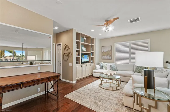 Living room with ceiling fan, healthy amount of natural light, dark wood-type flooring, and built in shelves