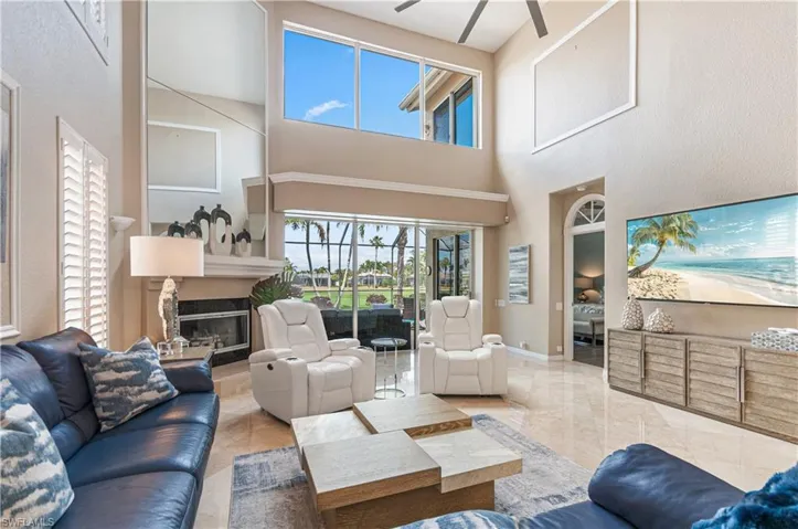 Living room featuring a glass covered fireplace, a high ceiling, and ceiling fan