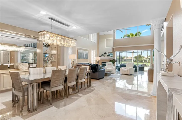 Dining space featuring a fireplace, light marble finish flooring, hanging lights, and a high ceiling