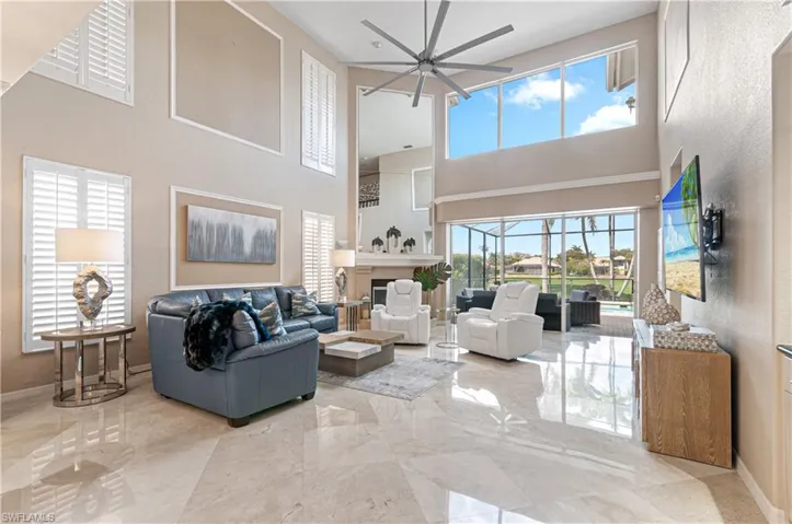 Living area featuring a ceiling fan, a fireplace, light marble finish flooring, and a high ceiling