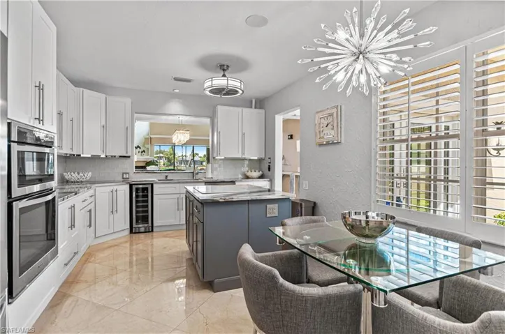 Two tone kitchen featuring a chandelier, two tone color scheme, wine cooler, stainless steel double oven, and light stone counters