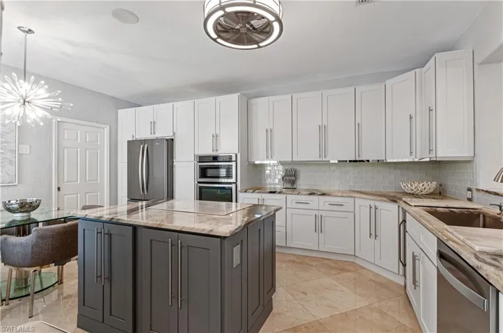 Kitchen with a center island, dual tone cabinets, light stone countertops, stainless steel appliances, and hanging lights