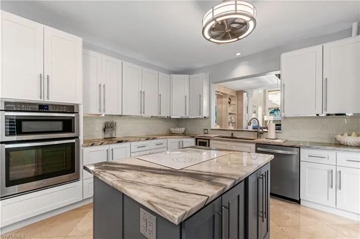 Kitchen featuring two tone cabinets, a center island, stainless steel appliances, light stone countertops, and light tile patterned flooring