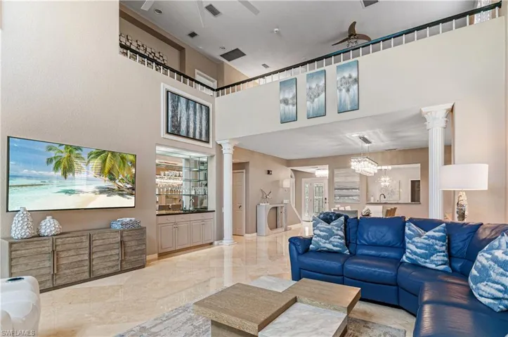 Living area featuring ornate columns, bar with sink, a high ceiling, ceiling fan, and light marble finish floors