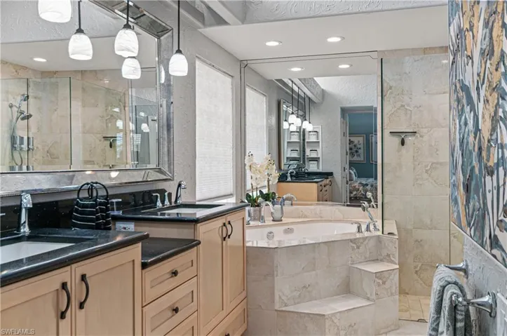 Full bathroom with two vanities, a bath, a tile shower, recessed lighting, and a textured wall