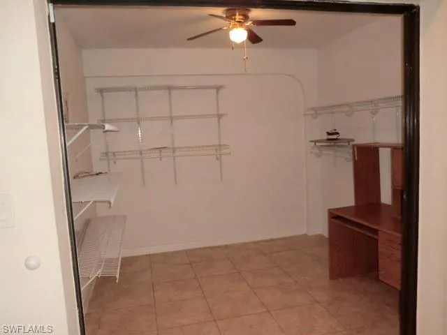 Room featuring tile flooring, white walls, built-in shelving, and a ceiling fan with light fixture