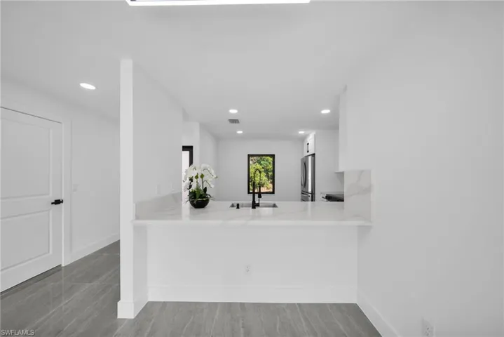 Kitchen featuring a peninsula, white cabinets, light stone counters, recessed lighting, and freestanding refrigerator