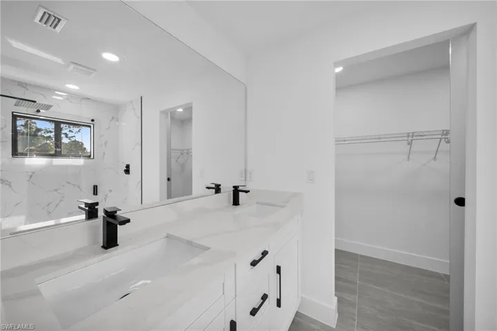 Full bath with a spacious closet, a marble finish shower, double vanity, and recessed lighting