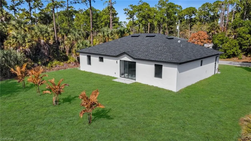 Rear view of house featuring a yard, a shingled roof, stucco siding, and view of scattered trees
