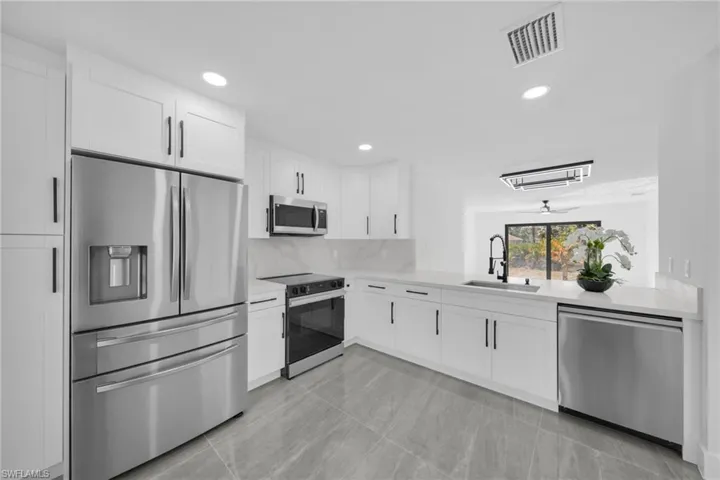 Kitchen with stainless steel appliances, white cabinetry, recessed lighting, light stone counters, and backsplash