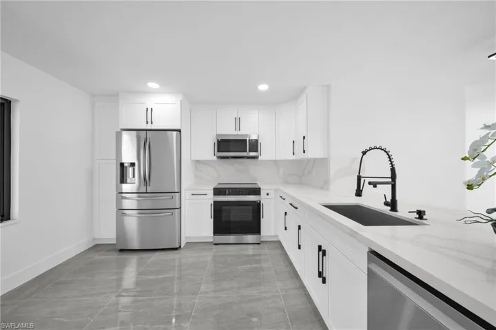 Kitchen featuring light stone counters, stainless steel appliances, white cabinets, decorative backsplash, and recessed lighting