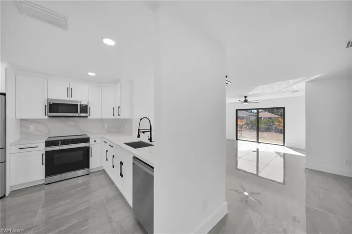 Kitchen featuring ceiling fan, white cabinets, stainless steel appliances, and light stone counters