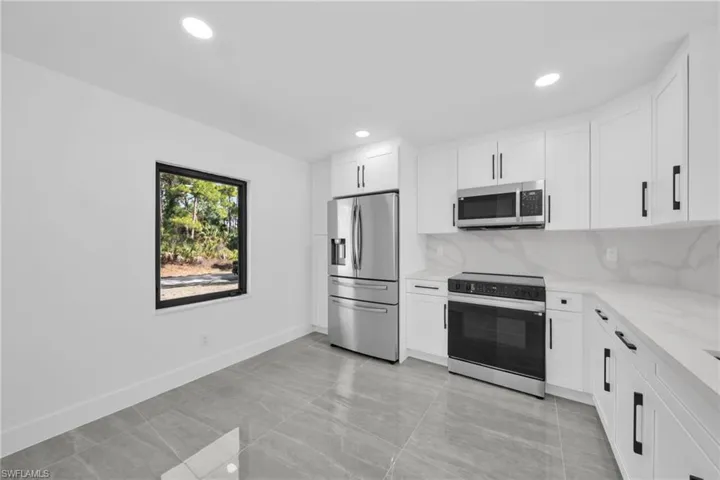 Kitchen featuring stainless steel appliances, white cabinets, light stone counters, backsplash, and recessed lighting