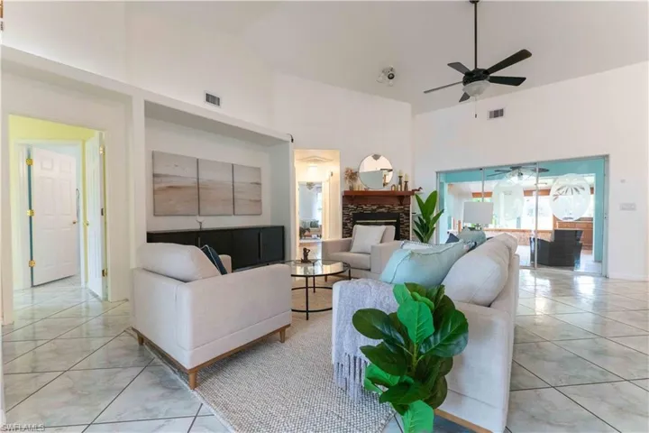 Living room with ceiling fan, high vaulted ceiling, and a stone fireplace