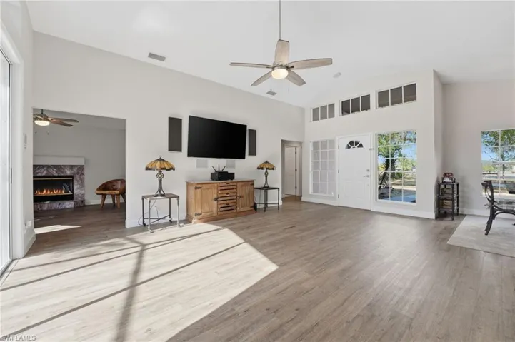 Living area with ceiling fan, a high end fireplace, light wood-style flooring, and high vaulted ceiling