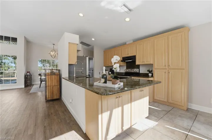 Kitchen with dark stone counters, a peninsula, light brown cabinets, electric range, and recessed lighting