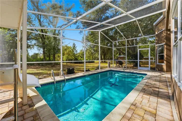 Swimming pool featuring a patio, a lanai, a sunroom, and view of scattered trees