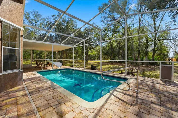 Outdoor pool with a patio, a sunroom, glass enclosure, a water slide, and view of scattered trees