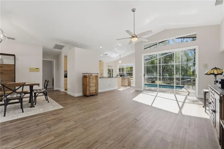 Living area with a sunroom, high vaulted ceiling, light wood-type flooring, and a ceiling fan