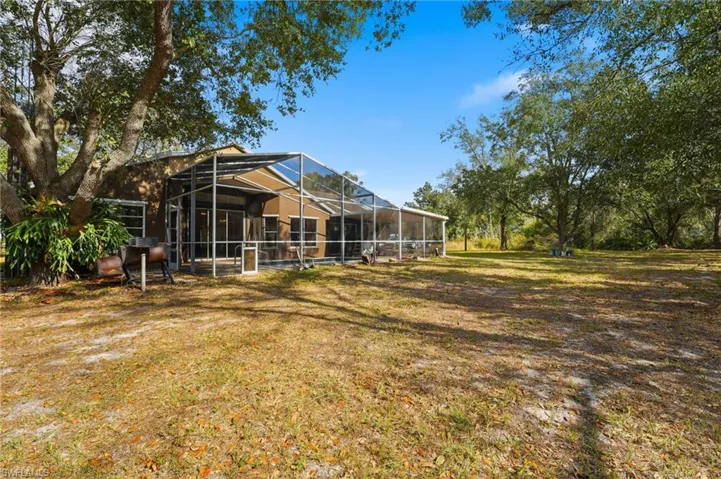 View of grassy yard featuring glass enclosure and a sunroom