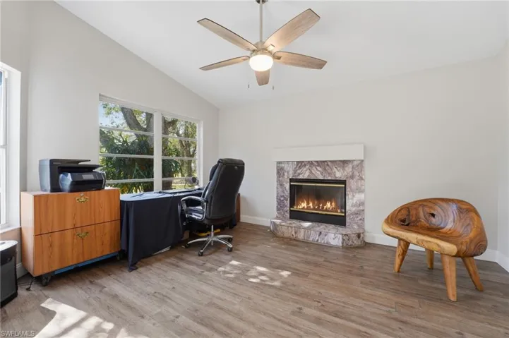 Office featuring lofted ceiling, a fireplace, light wood-type flooring, and a ceiling fan