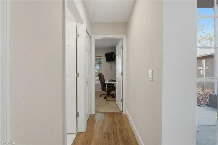 Hallway with an office area, light wood-style floors, and a textured wall