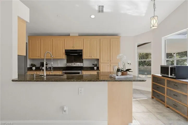 Kitchen featuring a peninsula, stainless steel appliances, dark stone counters, decorative light fixtures, and light tile patterned floors