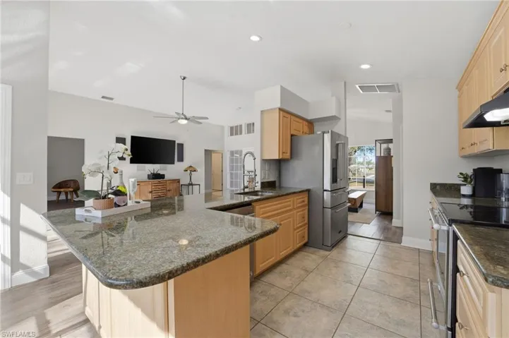 Kitchen with stainless steel appliances, a peninsula, dark stone countertops, ceiling fan, and lofted ceiling