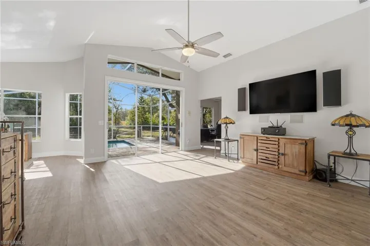 Living area with a sunroom, light wood-style flooring, a ceiling fan, and high vaulted ceiling